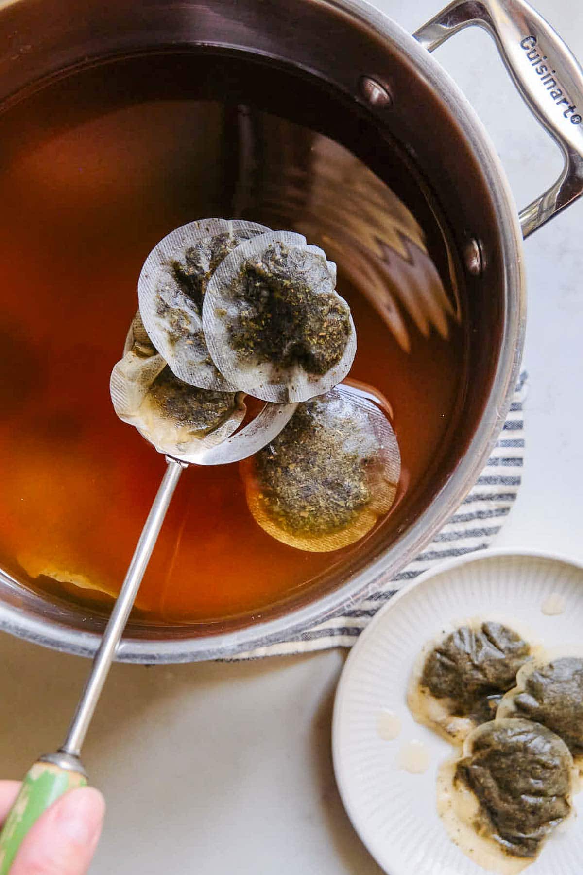 using spoon to scoop out tea bags from large pot.
