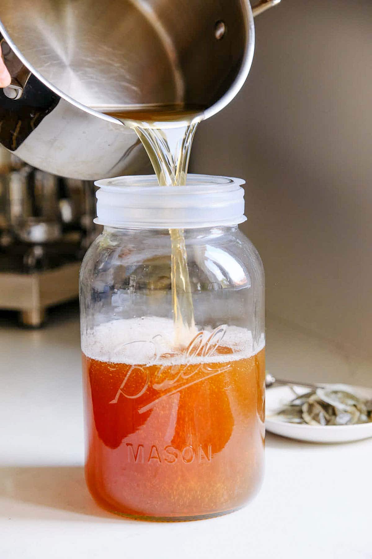 pouring pot of tea into large mason jar.