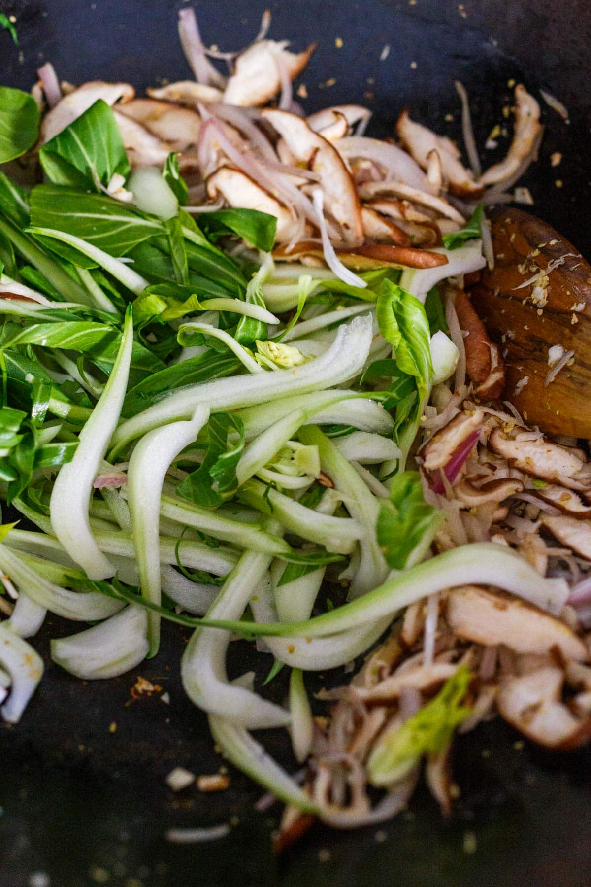 sliced bok choy added to wok with sautéed shiitake mushrooms, shallots.