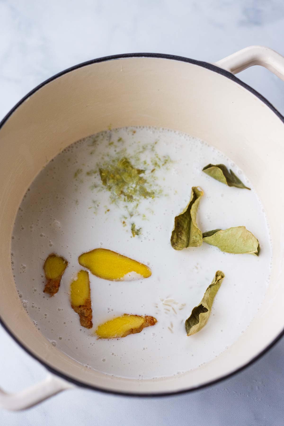 pot of uncooked jasmine rice, coconut milk, ginger slices, lemongrass, and lime leaves.