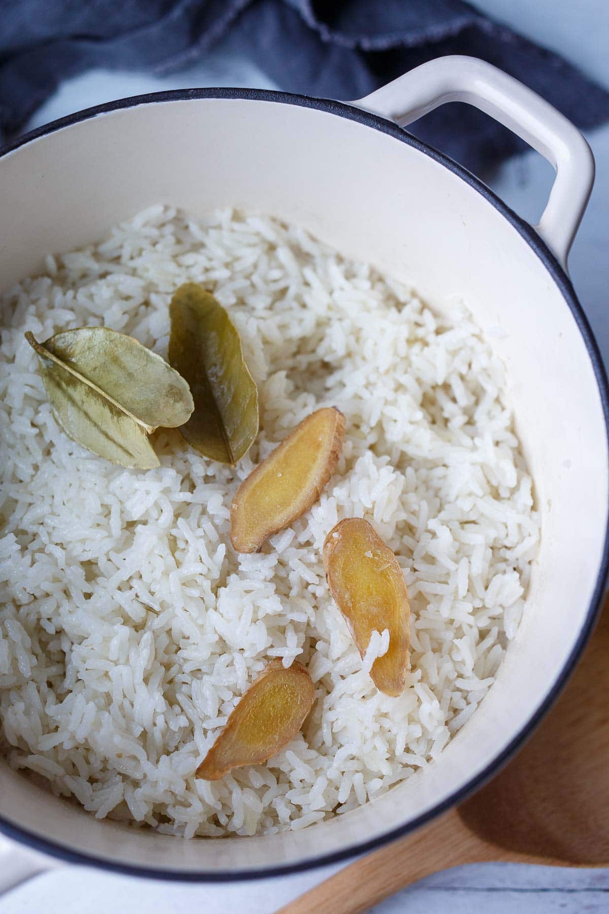 cooked coconut rice with dried lime leaves and fresh ginger slices on top.