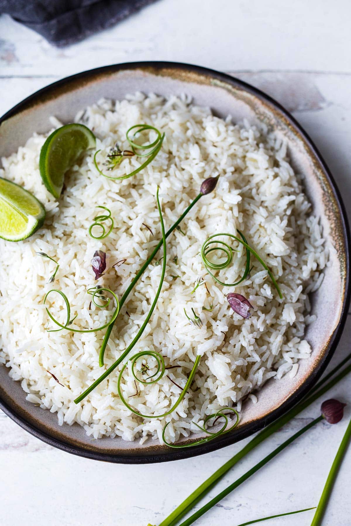 bowl of cooked coconut rice, garnished with lime wedges and chive blossoms.