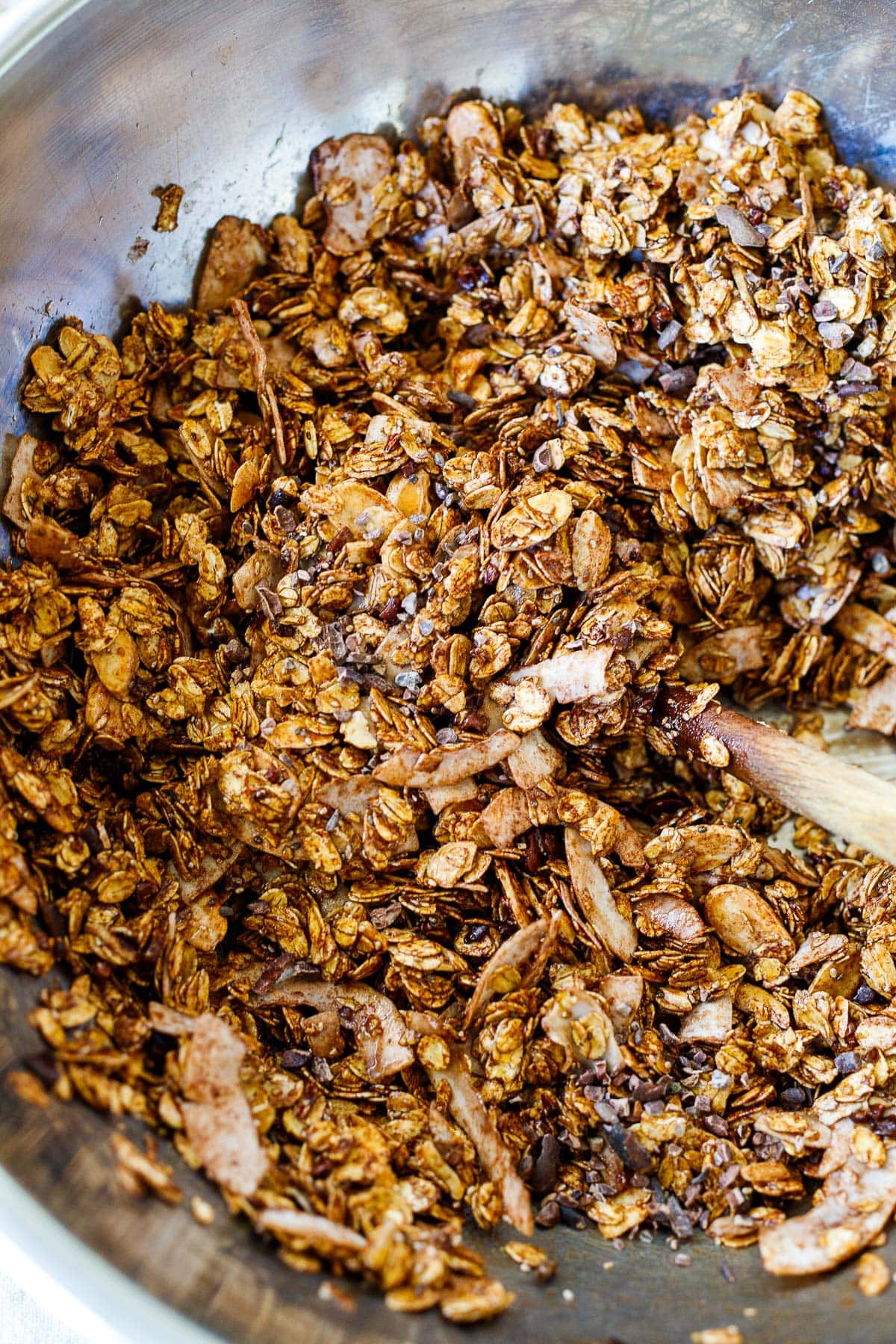 mixing bowl with ingredients for dark chocolate granola mixed together with wood spoon.