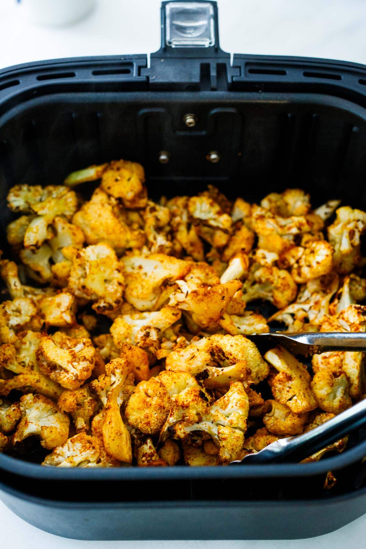 cauliflower florets in air fryer, tossed with tongs. 