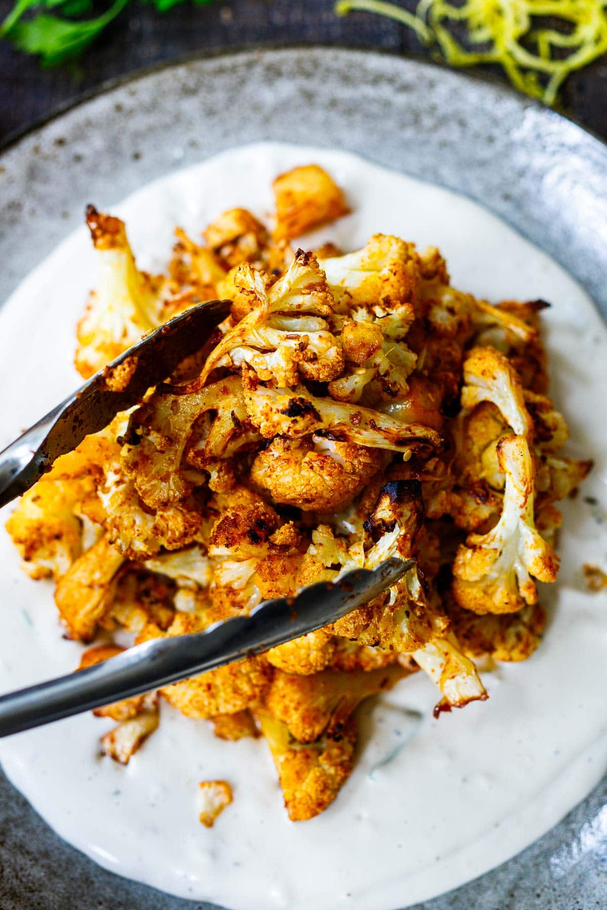 tongs placing air fryer crispy cauliflower onto plate with yogurt tahini sauce. 
