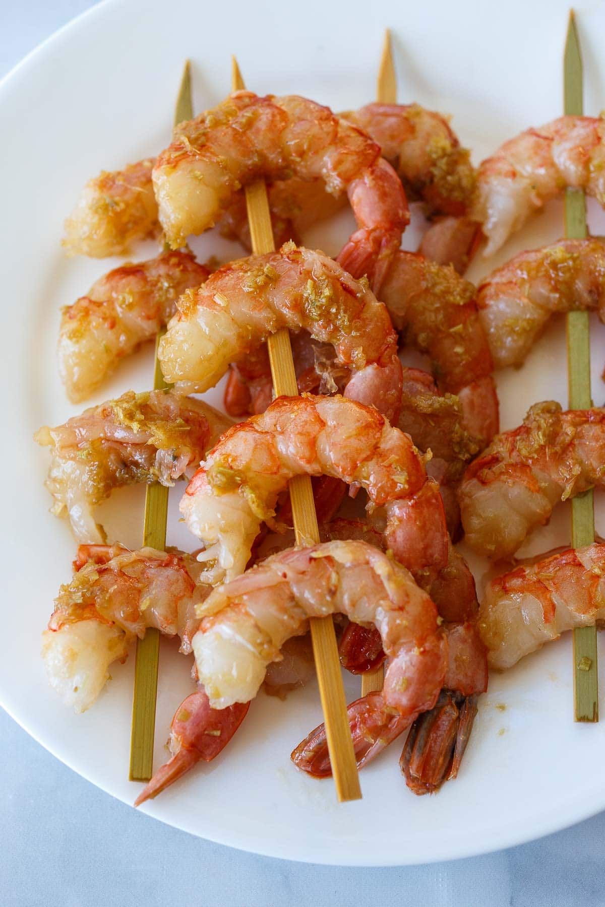 raw, marinated lemongrass shrimp on skewers on plate.