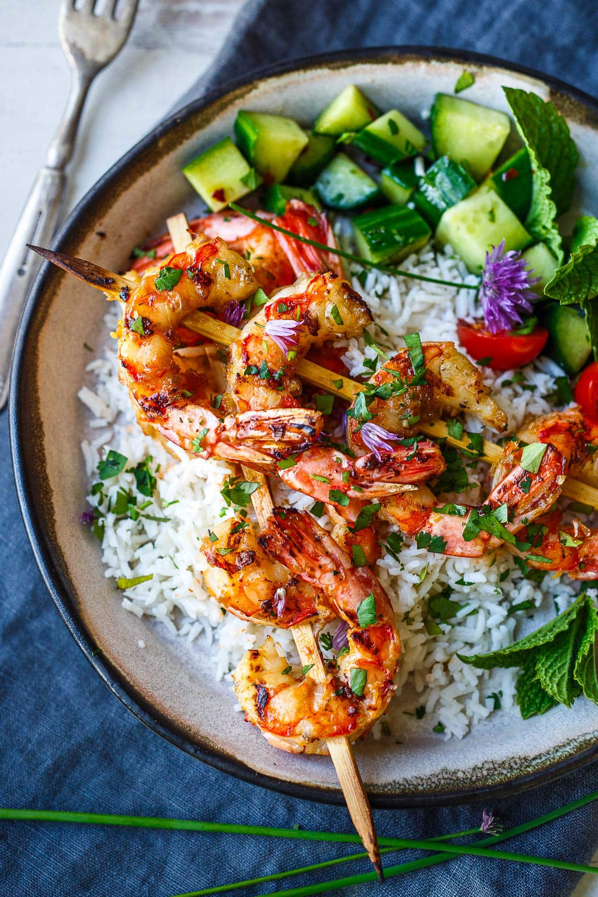 coconut rice bowl with grilled lemongrass shrimp skewers, garnished with fresh herbs and chive blossoms. 