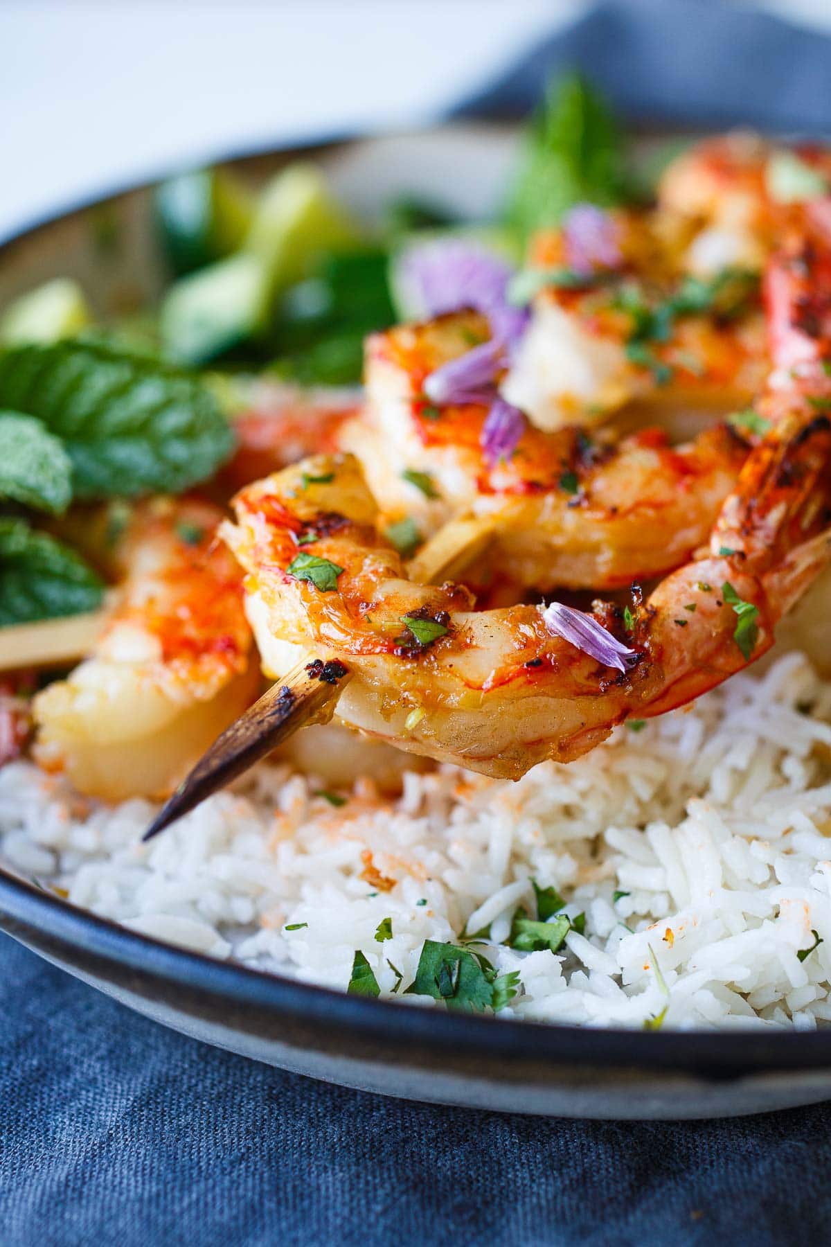 grilled lemongrass shrimp on skewer with fresh herbs and chive blossom garnish.