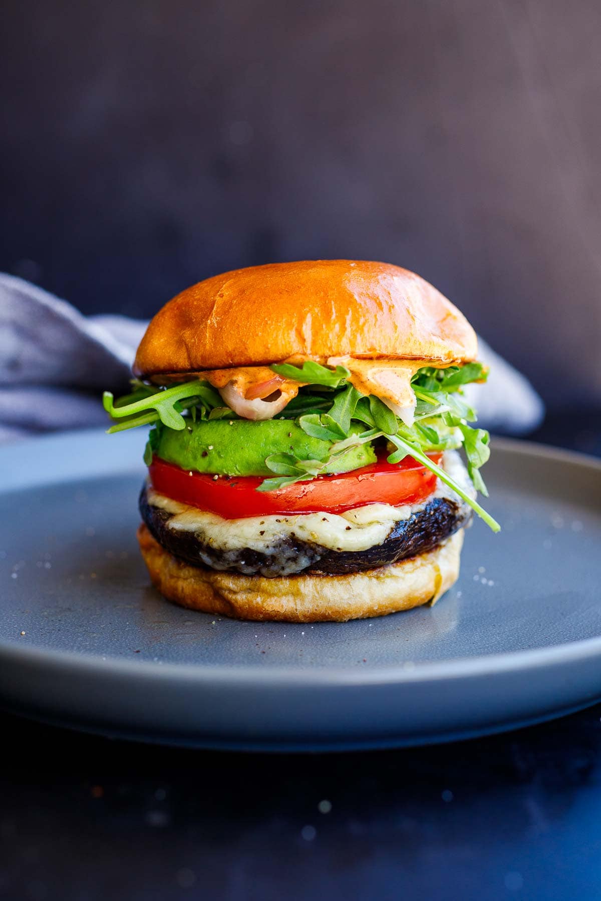 portobello mushroom burger on brioche bun with melted cheese, sliced tomato and avocado, arugula, and chipotle mayo sauce.