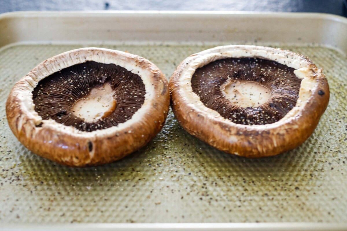 portobello mushrooms gill-side up on baking sheet, seasoned with oil, salt, and pepper.