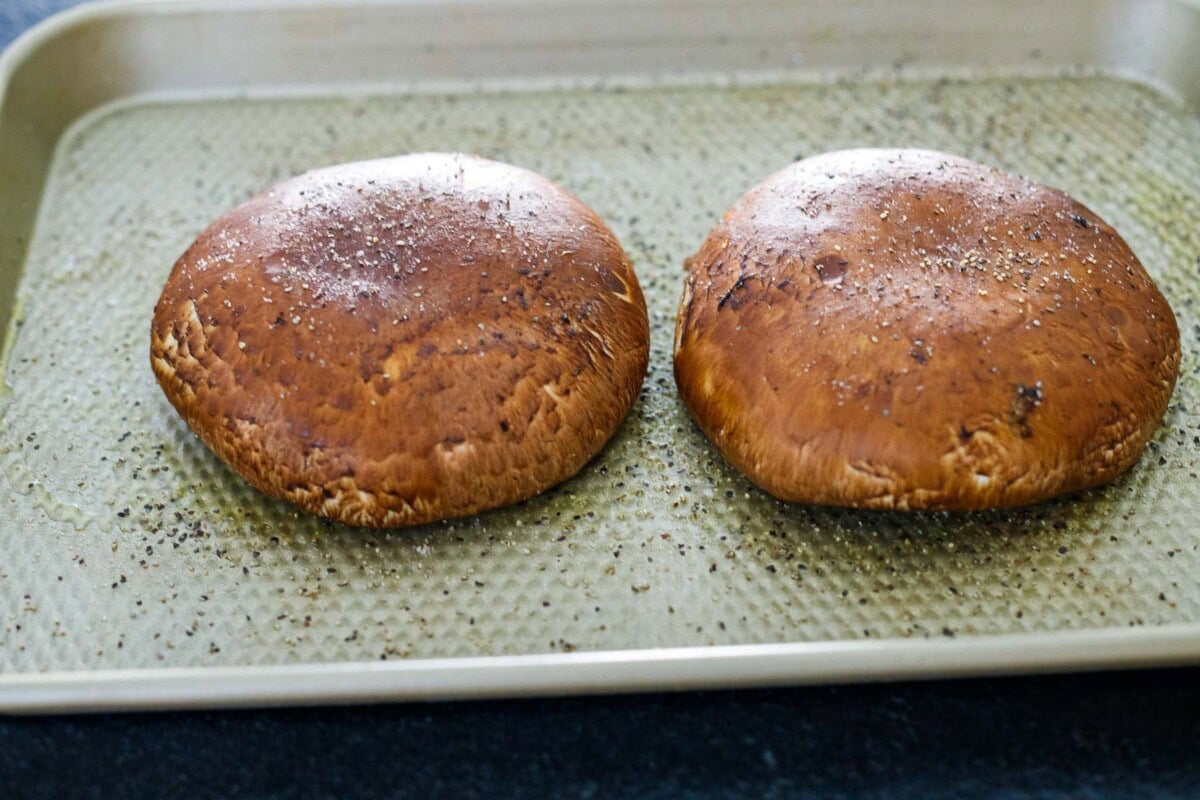 two portobello mushrooms gill-side down on baking sheet, seasoned with oil, salt, and pepper.