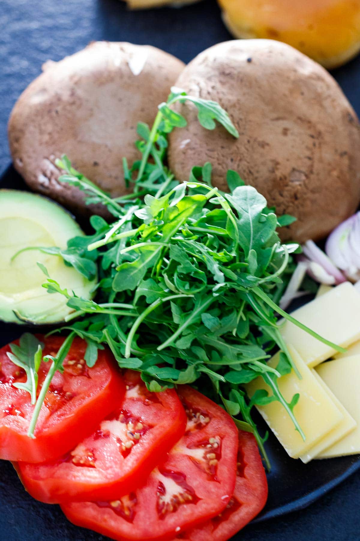 portobello burger fixings on plate - mushrooms, onions, cheese, tomato, avocado, arugula.