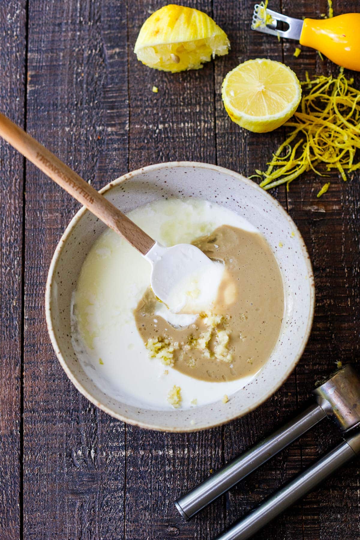 bowl with ingredients for tahini yogurt sauce and spatula - greek yogurt, tahini, garlic, lemon, oil.
