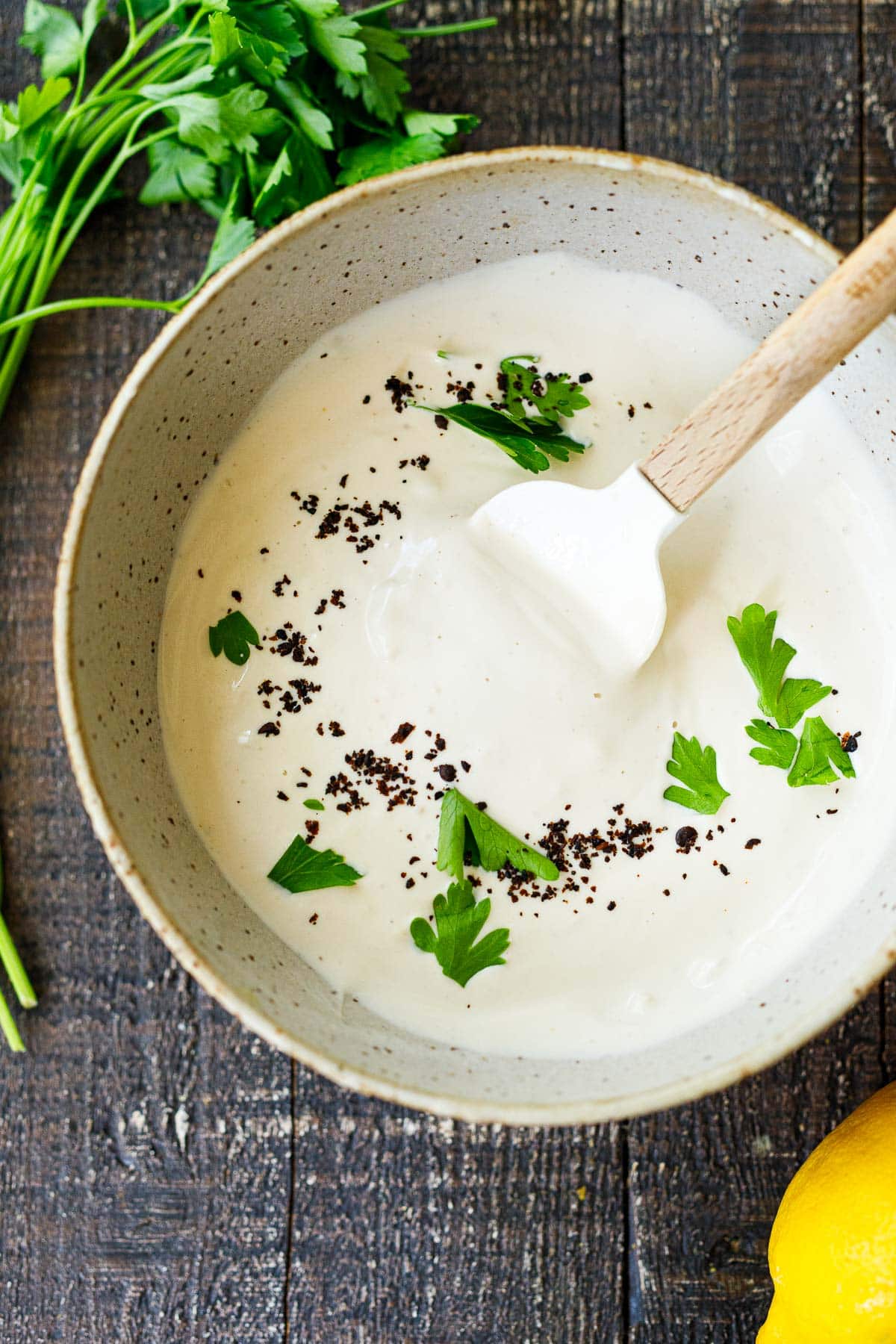bowl with spatula and tahini yogurt sauce garnished with parsley and aleppo chili flakes.