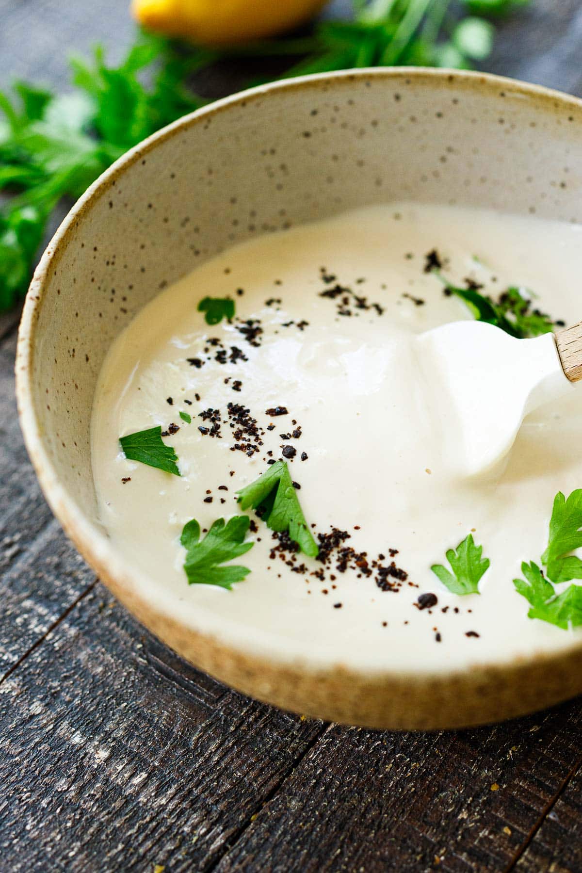 bowl with tahini yogurt sauce garnished with parsley and Aleppo chili flakes.