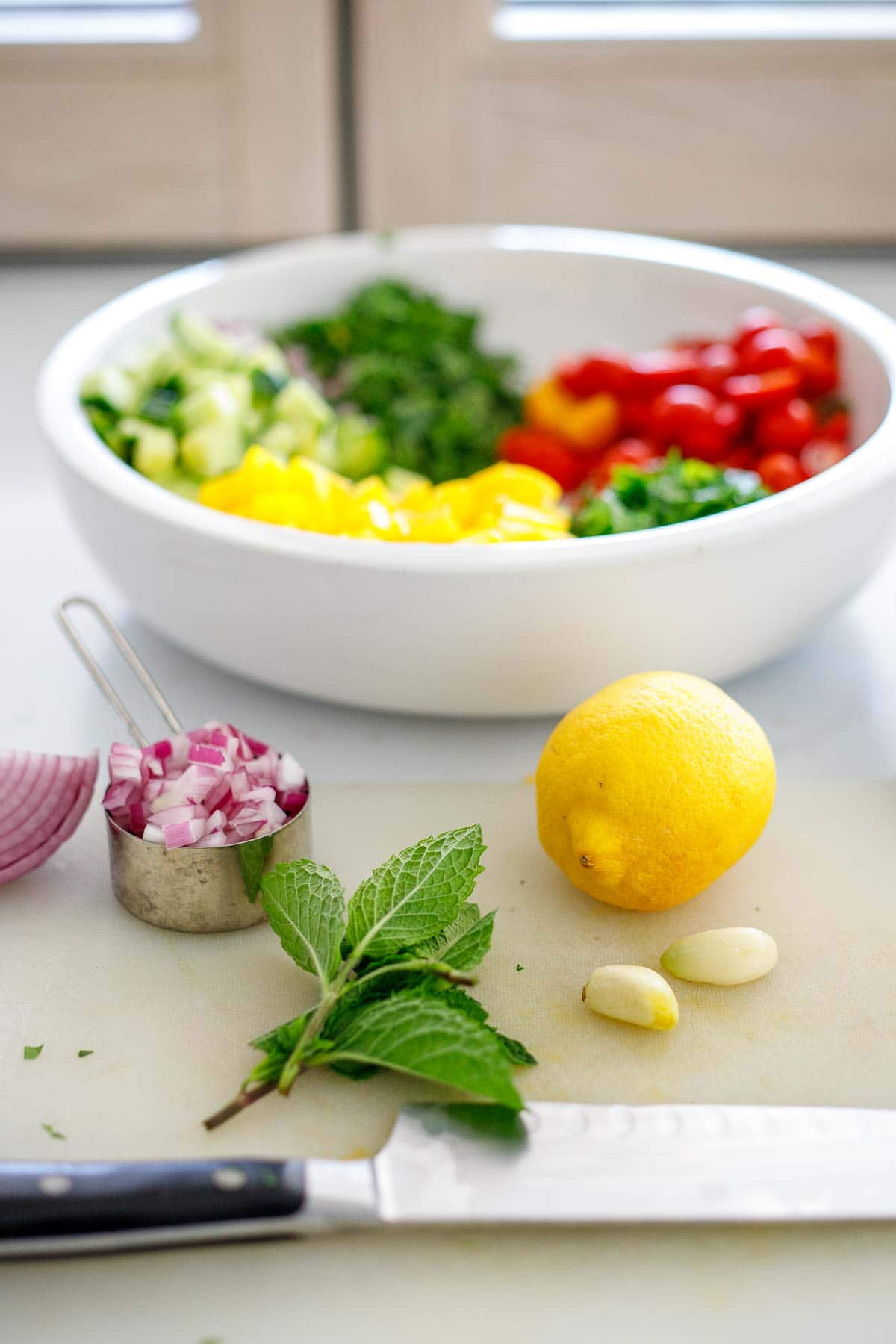 lentil salad ingredients- lemon, garlic cloves, minced red onion in measuring cup, mint bunch, and sharp knife.