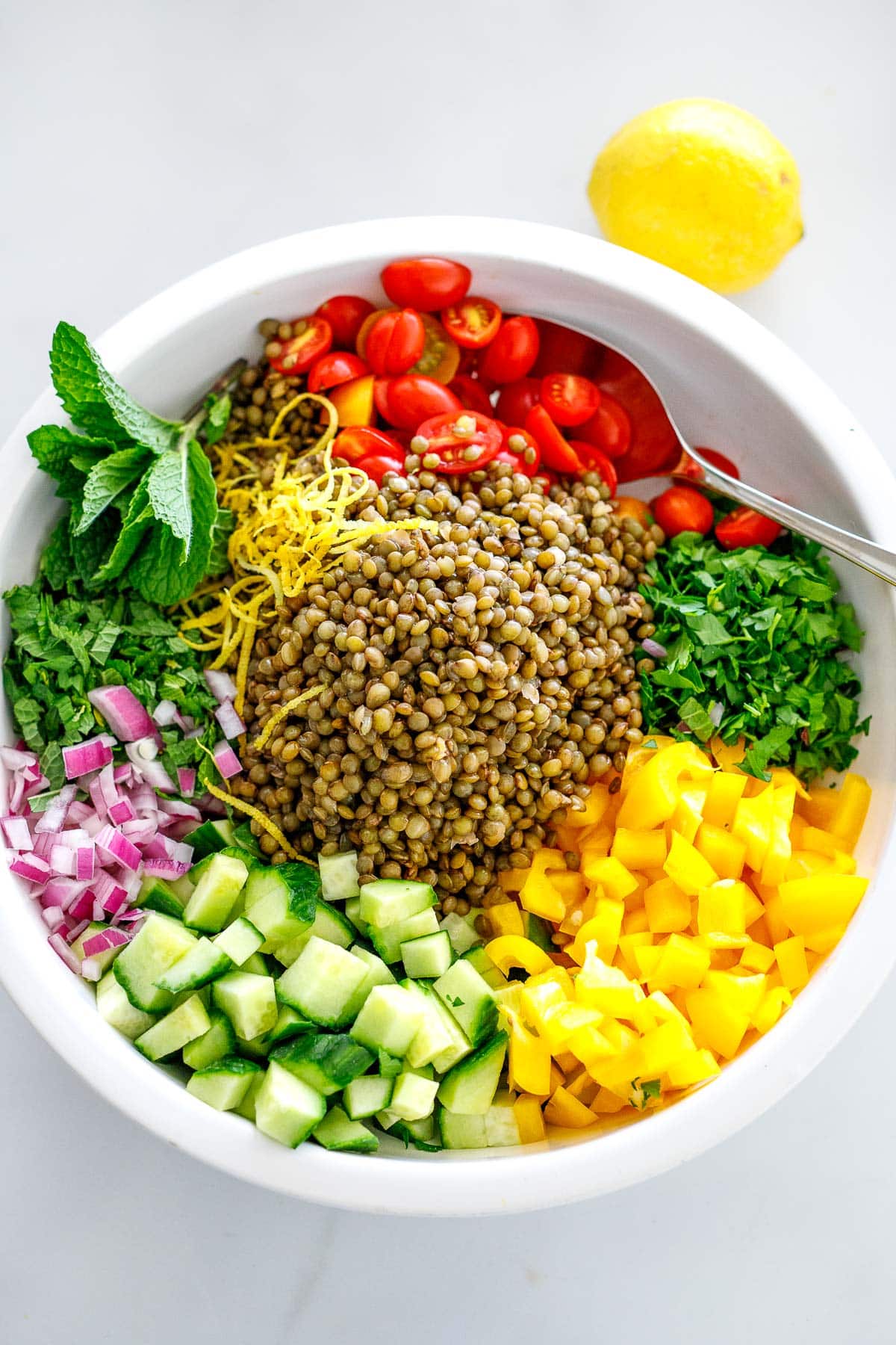 lentil salad components in bowl - lentils, cherry tomatoes, herbs, peppers, cucumbers, red onion, and lemon zest.