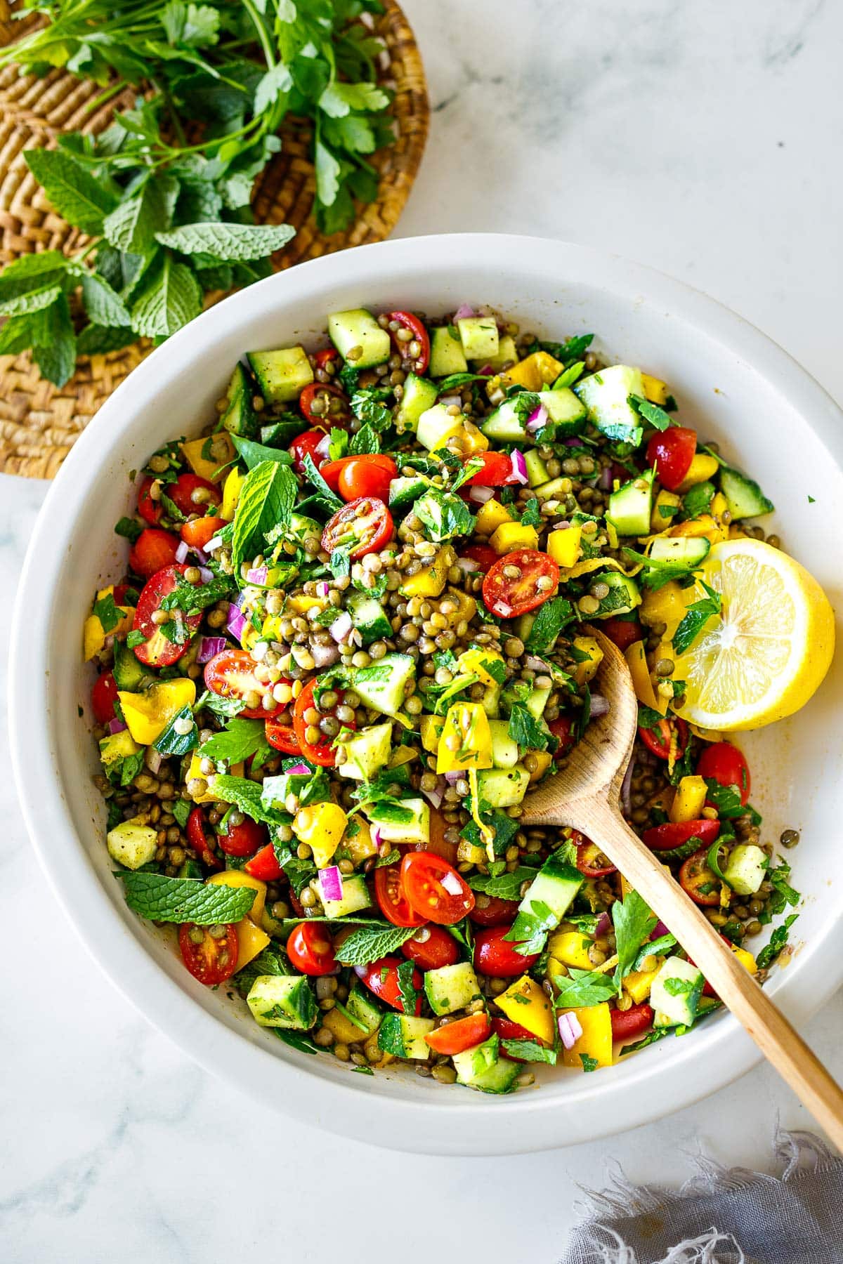 lentil salad in large bowl with lemon half, topped with herbs and lemon zest.