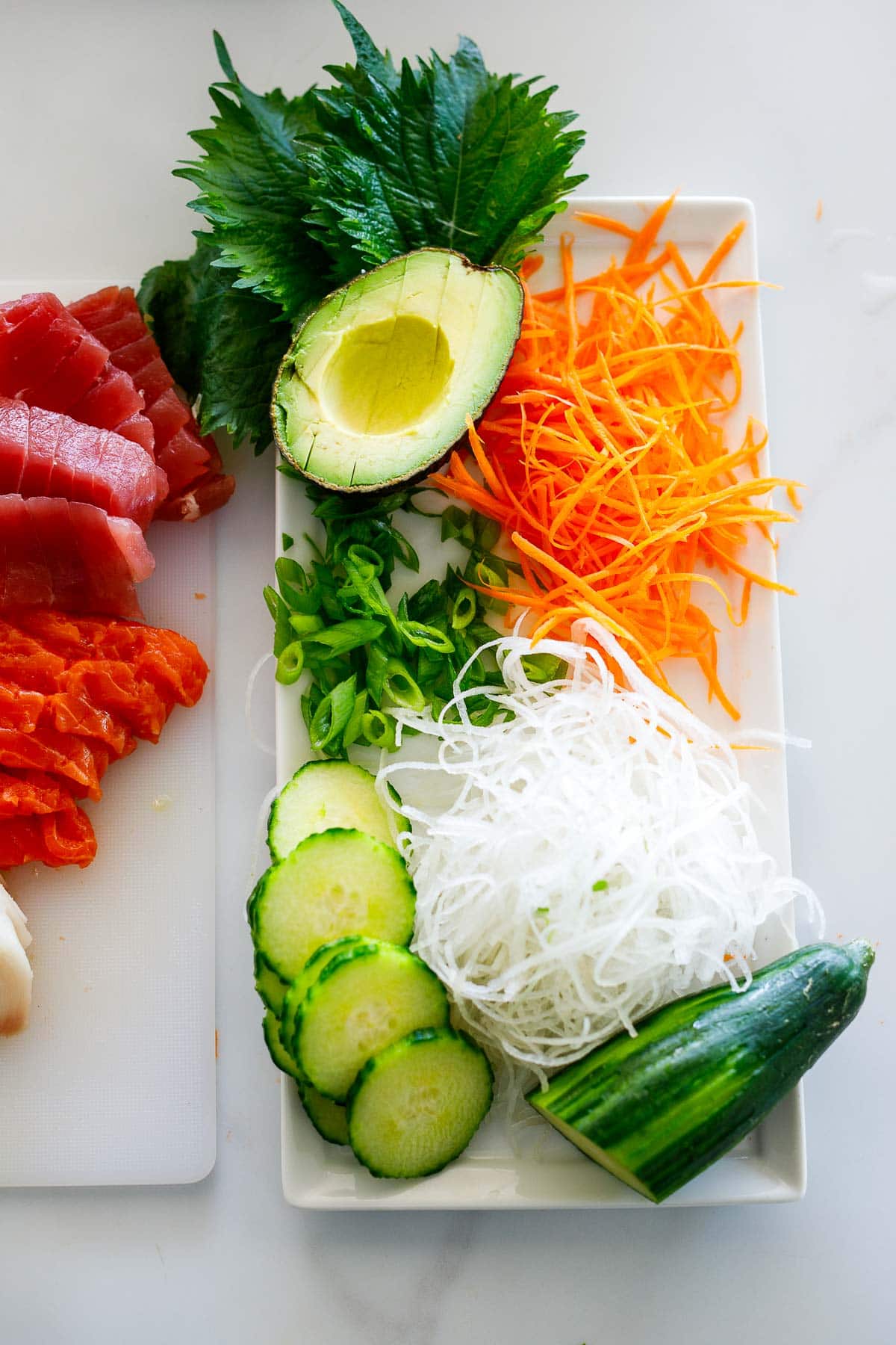 plate with raw veggies - sliced cucumber, grated daikon and carrots, green onions, shiso leaves, and avocado half.