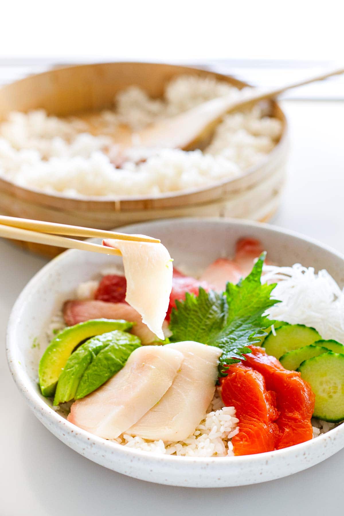 chopsticks placing slice of fish on chirashi bowl.