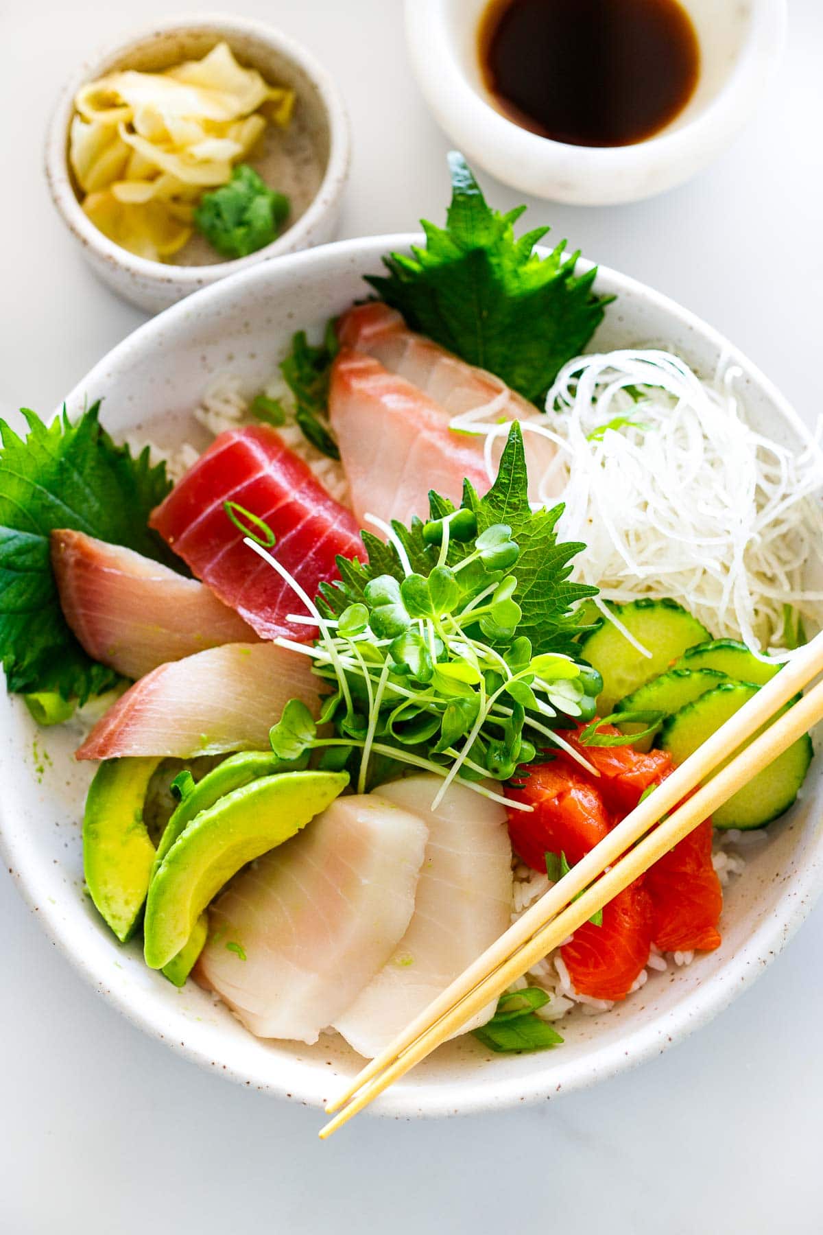 chirashi sushi bowl with sliced fish, sliced cucumber and avocado, herbs, sprouts, and grated daikon.
