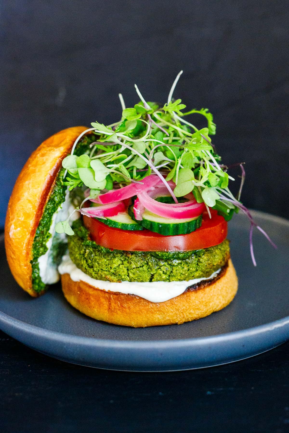 A falafel burger with pickled onions, tomatoes, cucumber and and tahini yogurt, zhoug, on a plate.
