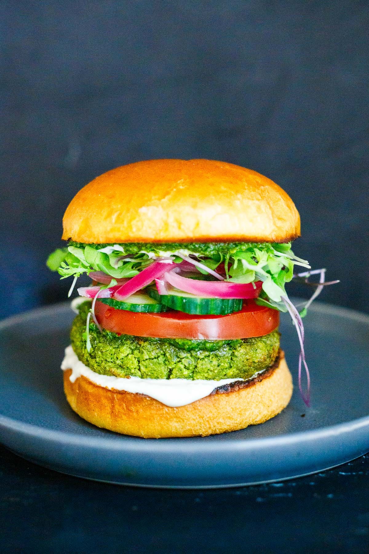 A falafel burger on a plate with all the fixings.