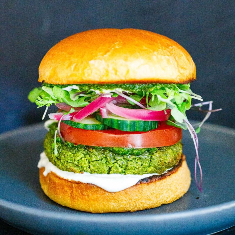 This falafel burger is a punchy, flavorful, high-protein vegetarian dinner! Top with tahini yogurt, pickled onions, sliced cucumbers, and tomatoes on a toasty brioche bun.