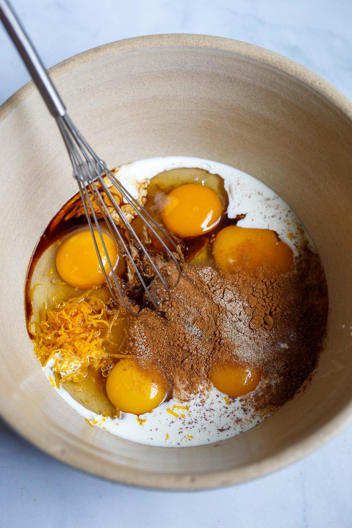 mixing bowl and whisk with eggs, orange zest, vanilla, cinnamon, nutmeg, whole milk, and heavy cream. 