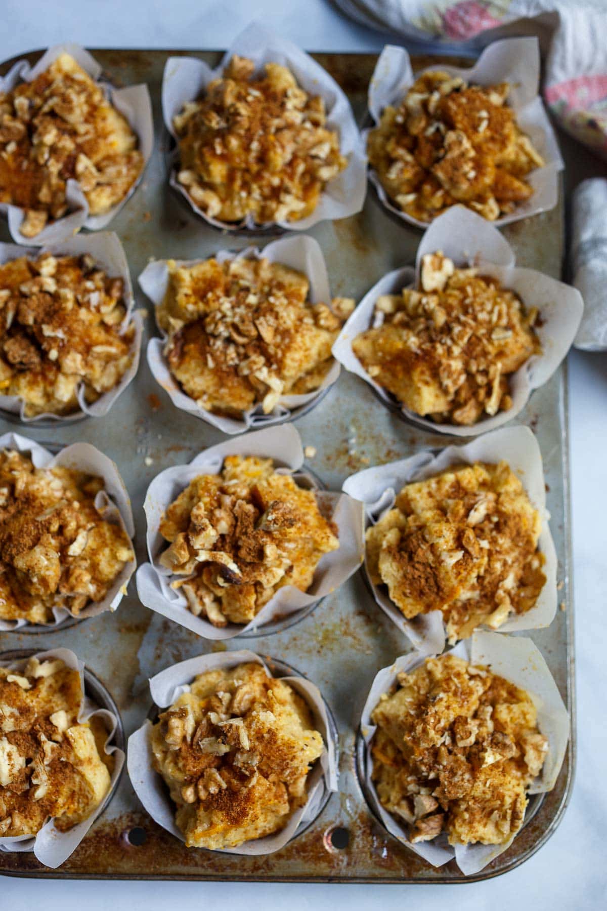 muffin pan with French toast muffins in paper liners, topped with nuts and cinnamon.