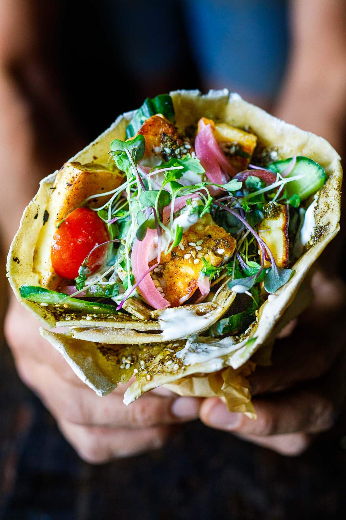 hands holding a cone-shaped halloumi wrap drizzled with tahini yogurt sauce.