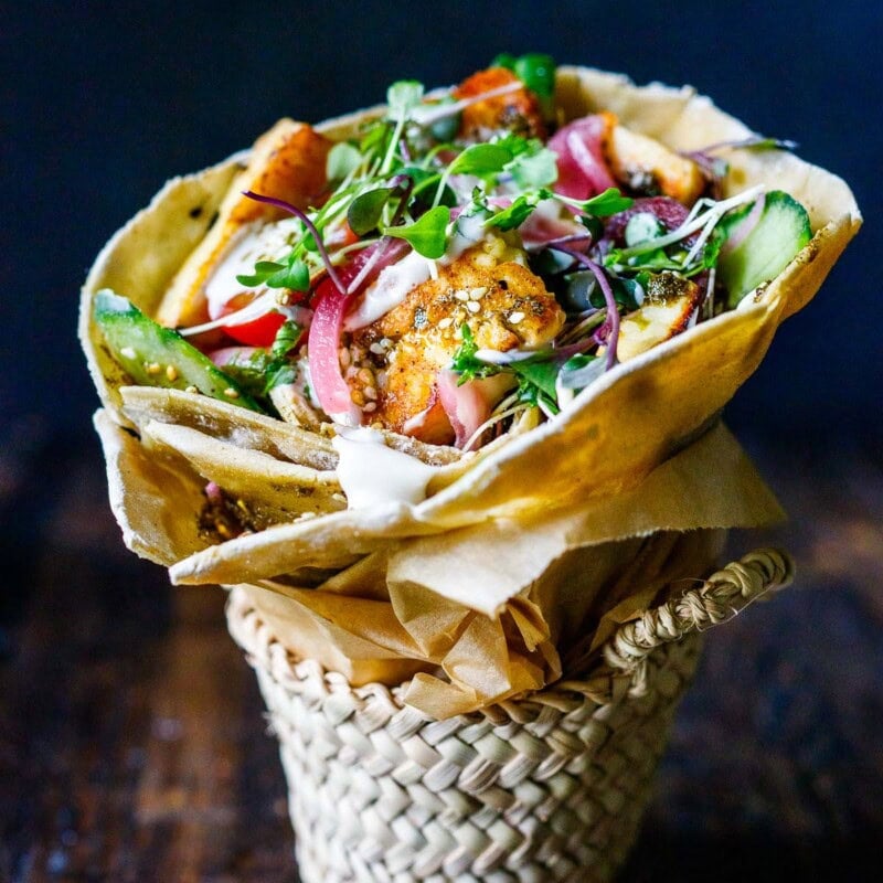 A delicious Halloumi Wrap recipe made with flavorful manoushe, pan-seared halloumi, fresh veggies, and a creamy tahini yogurt sauce.
