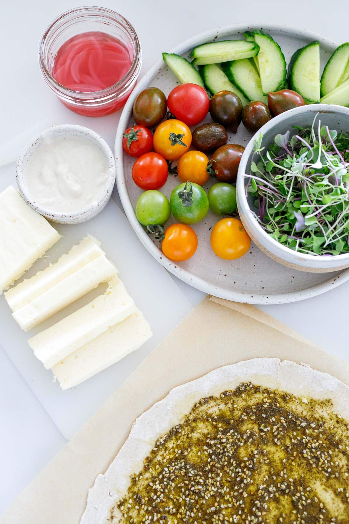 ingredients for halloumi wrap - cherry tomatoes, micro greens, tahini yogurt sauce, sliced halloumi, zaatar paste spread onto manoushe.