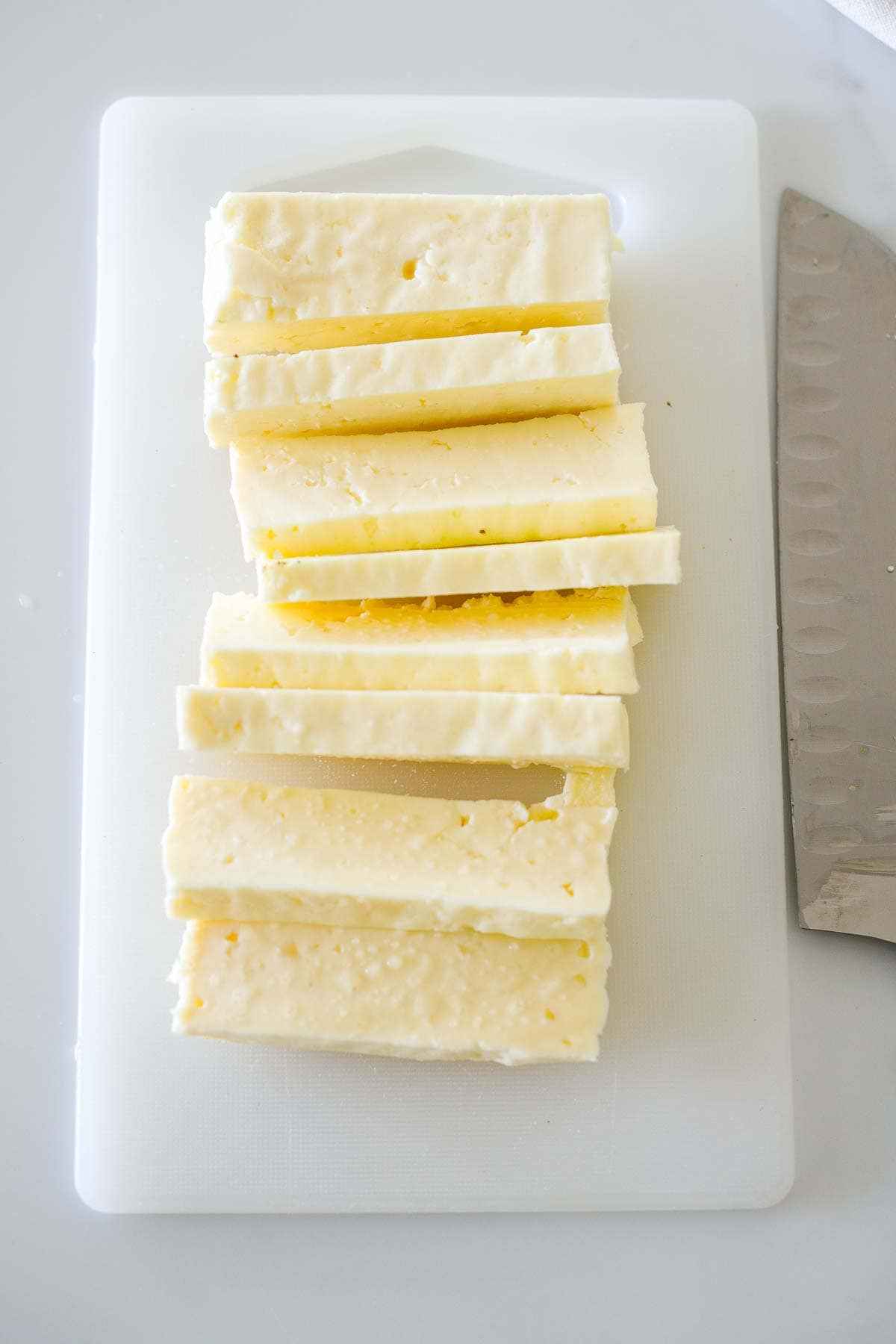sliced halloumi cheese on cutting board with sharp knife.