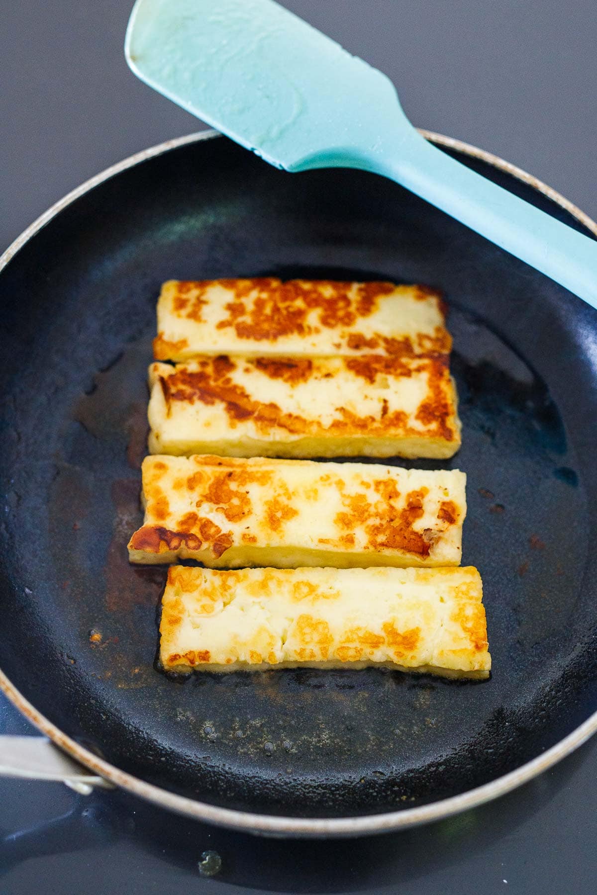 sliced halloumi cheese pan-searing in skillet.
