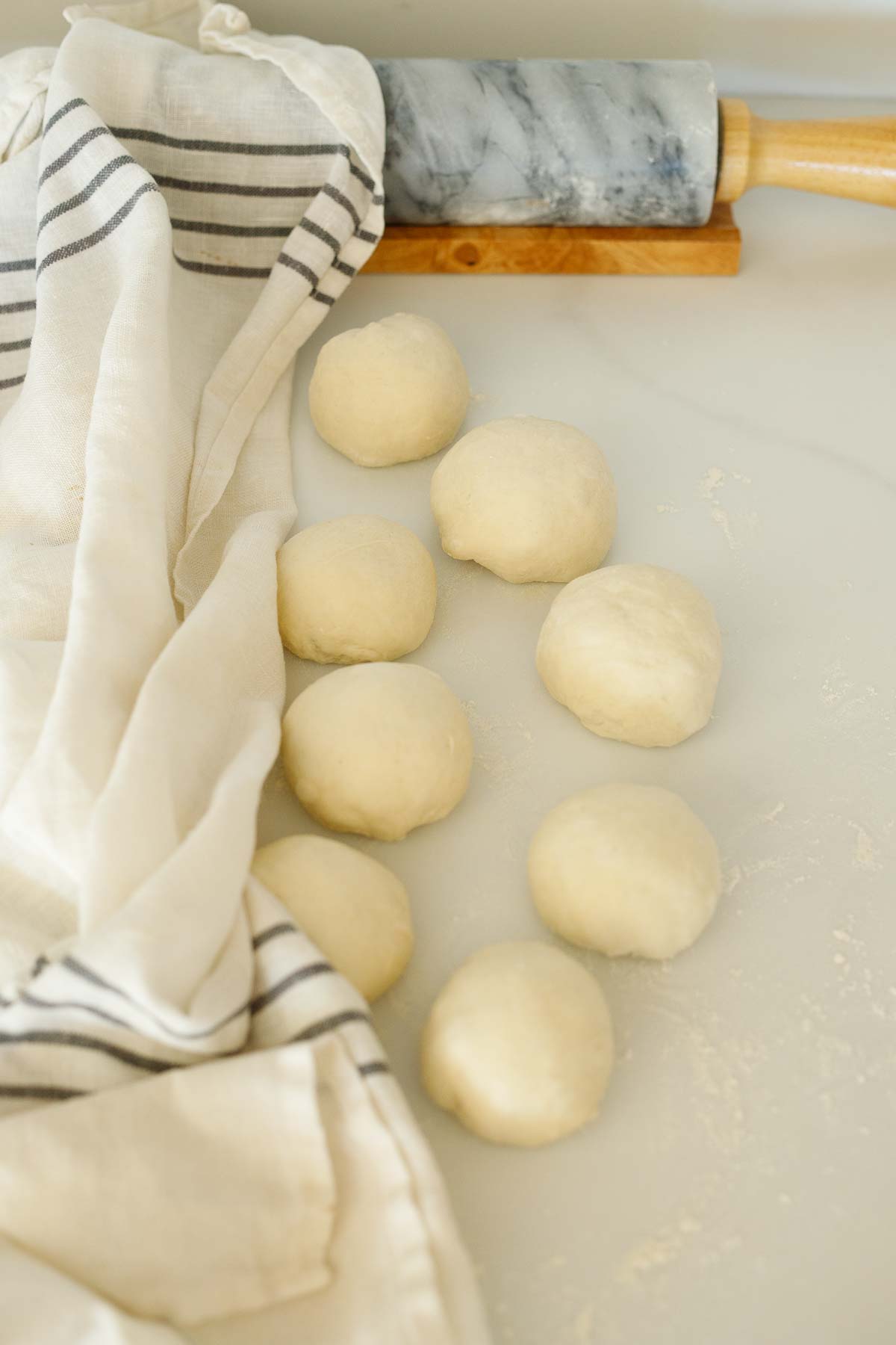 manoushe dough balls on surface near kitchen towel and rolling pin.
