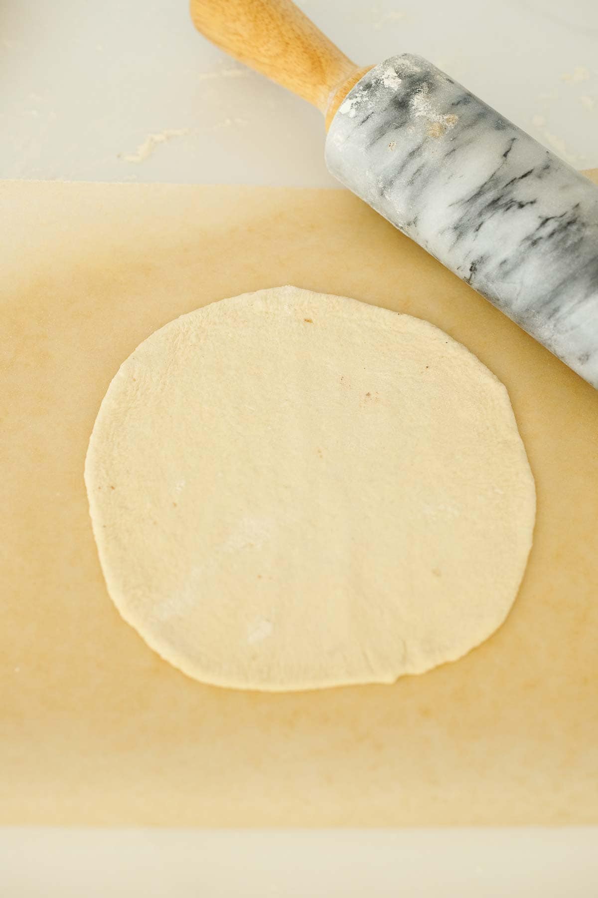 manoushe dough rolled out on parchment with rolling pin.