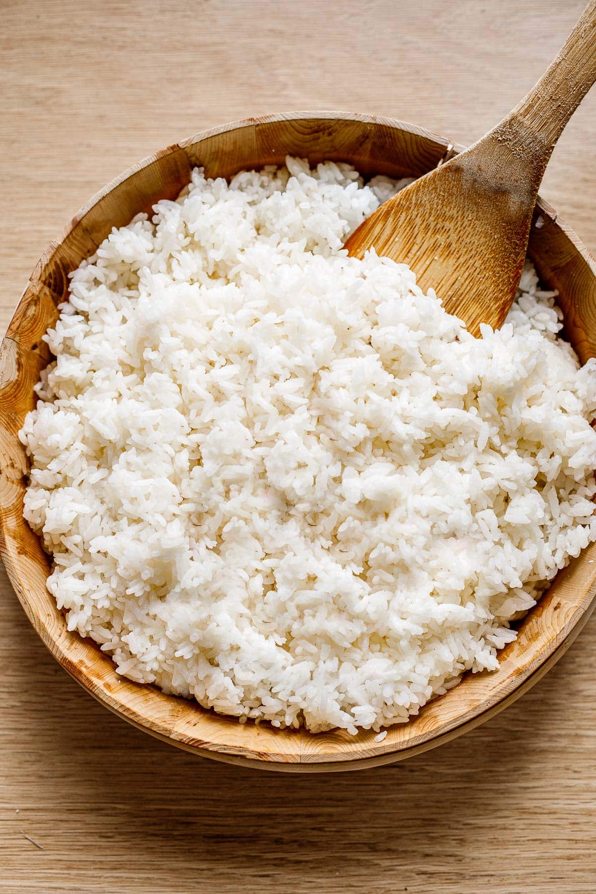 Sushi rice in a wooden bowl with a wooden paddle. 