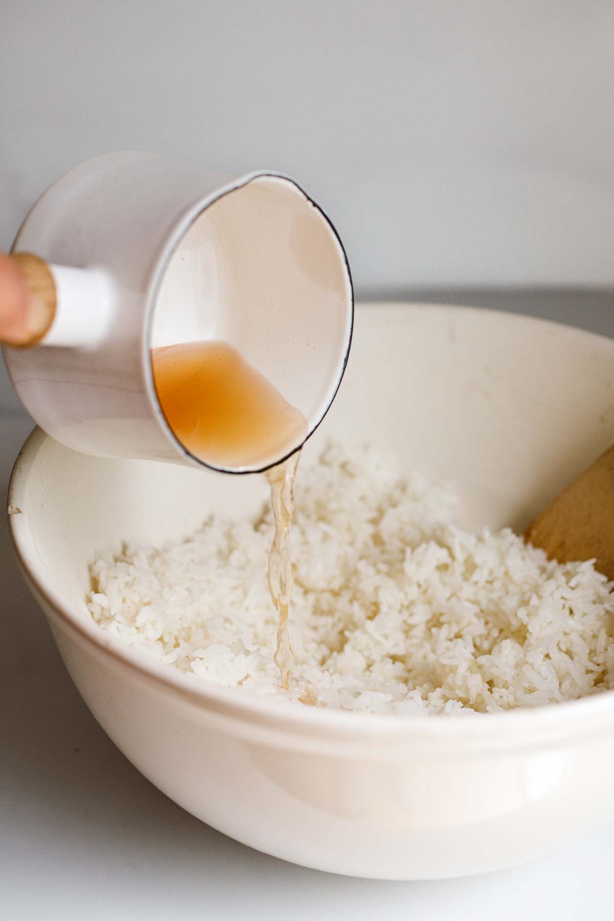 pouring vinegar mixture into bowl of sushi rice. 
