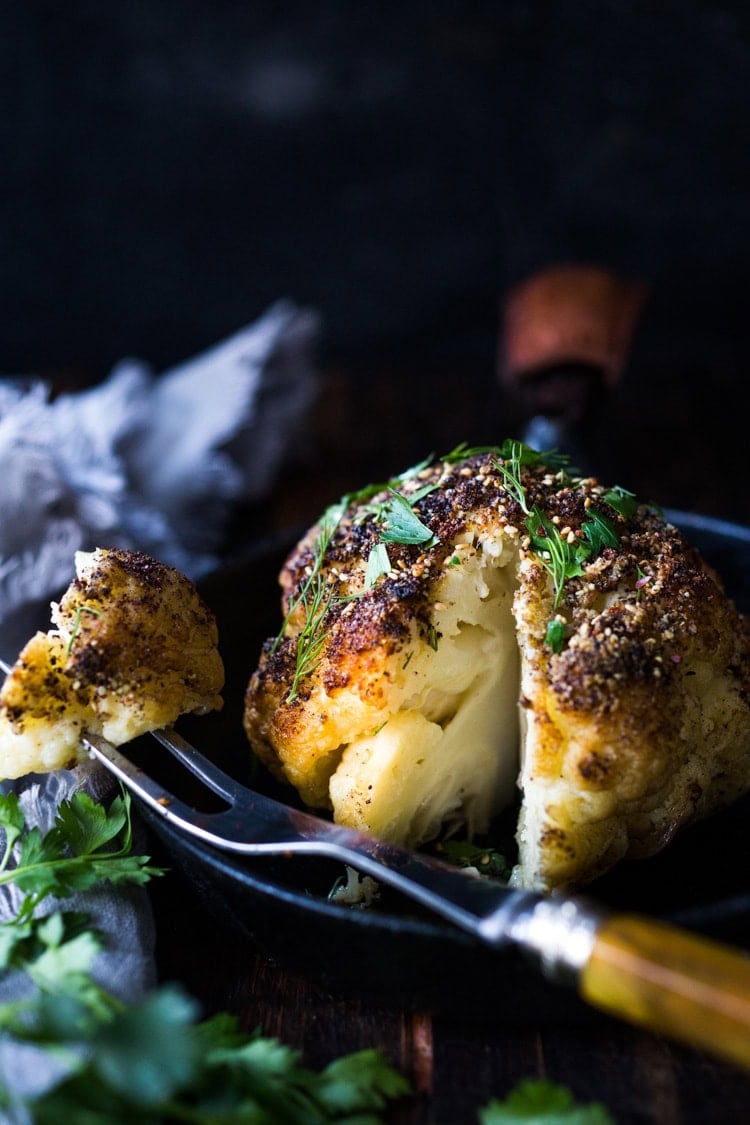 whole roasted cauliflower with zaatar and fresh herbs, fork holding wedge cut out of cauliflower head. 