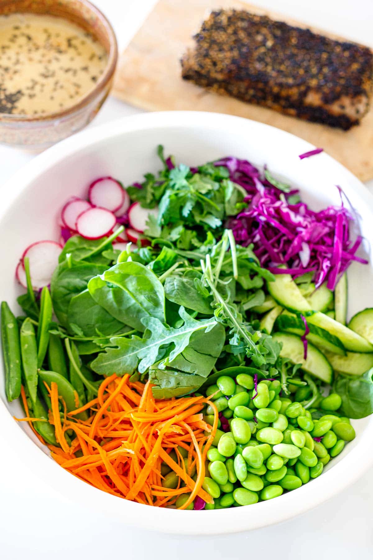 mixing bowl with fresh greens, grated carrots and cabbage, snap peas, edamame, cucumber, and radish. 