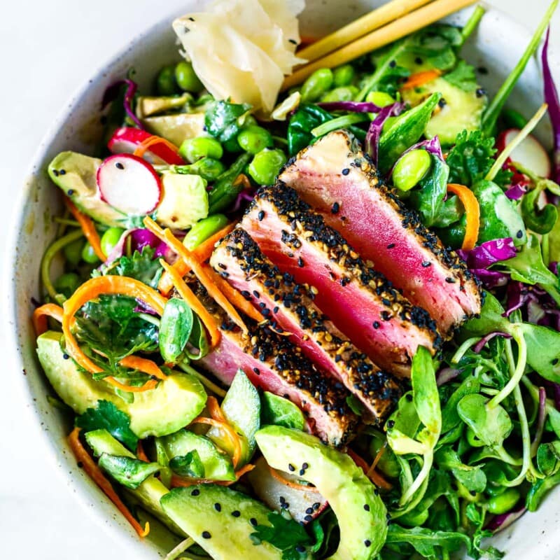 This sesame-crusted seared ahi tuna salad recipe is deliciously refreshing and light! Served over fresh greens with avocado, cucumber, edamame, grated carrots, cabbage, radishes, and sunflower sprouts tossed in a ginger wasabi dressing.