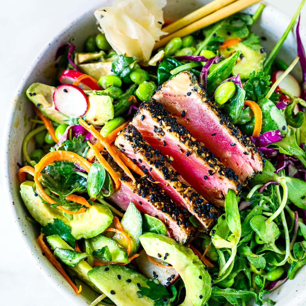 sesame crusted seared ahi tuna salad in a bowl with crunchy, colorful veggies, pickled ginger and chopsticks.