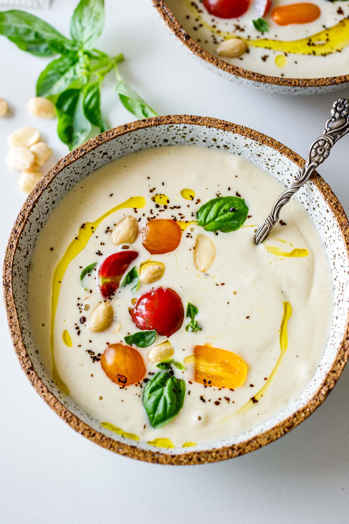 soup bowl with ajo blanco garnished with grape tomatoes, marcona almonds, basil, black pepper, and a drizzle of olive oil.