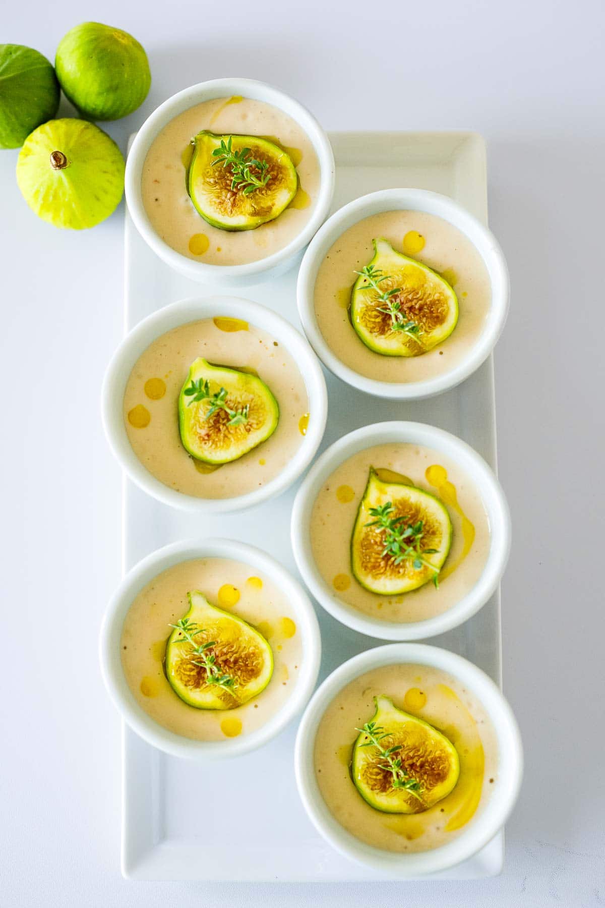 serving tray with appetizer bowls of ajo blanco garnished with figs, olive oil, and herbs. 