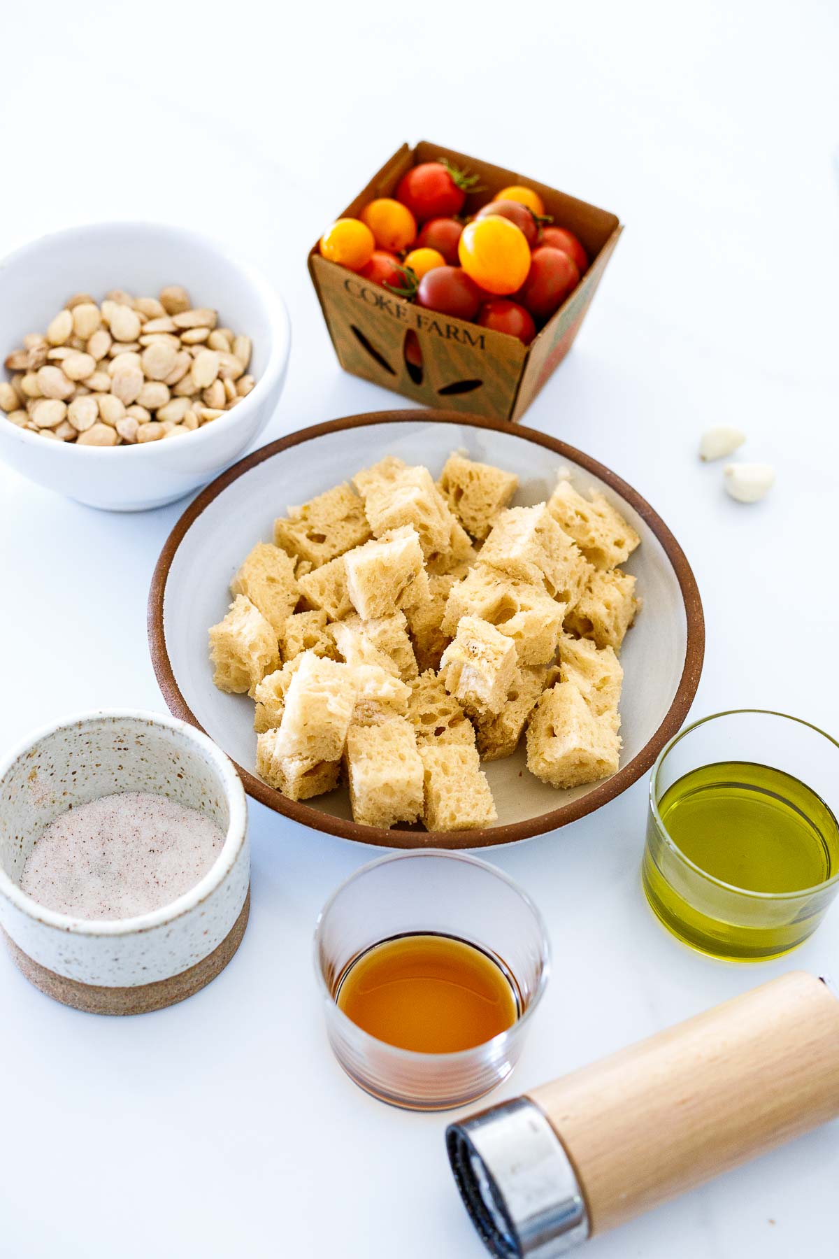 ingredients laid out for ajo blanco - grape tomatoes, marcona almonds, cubed bread, garlic cloves, olive oil, salt, vinegar, and pepper shaker. 