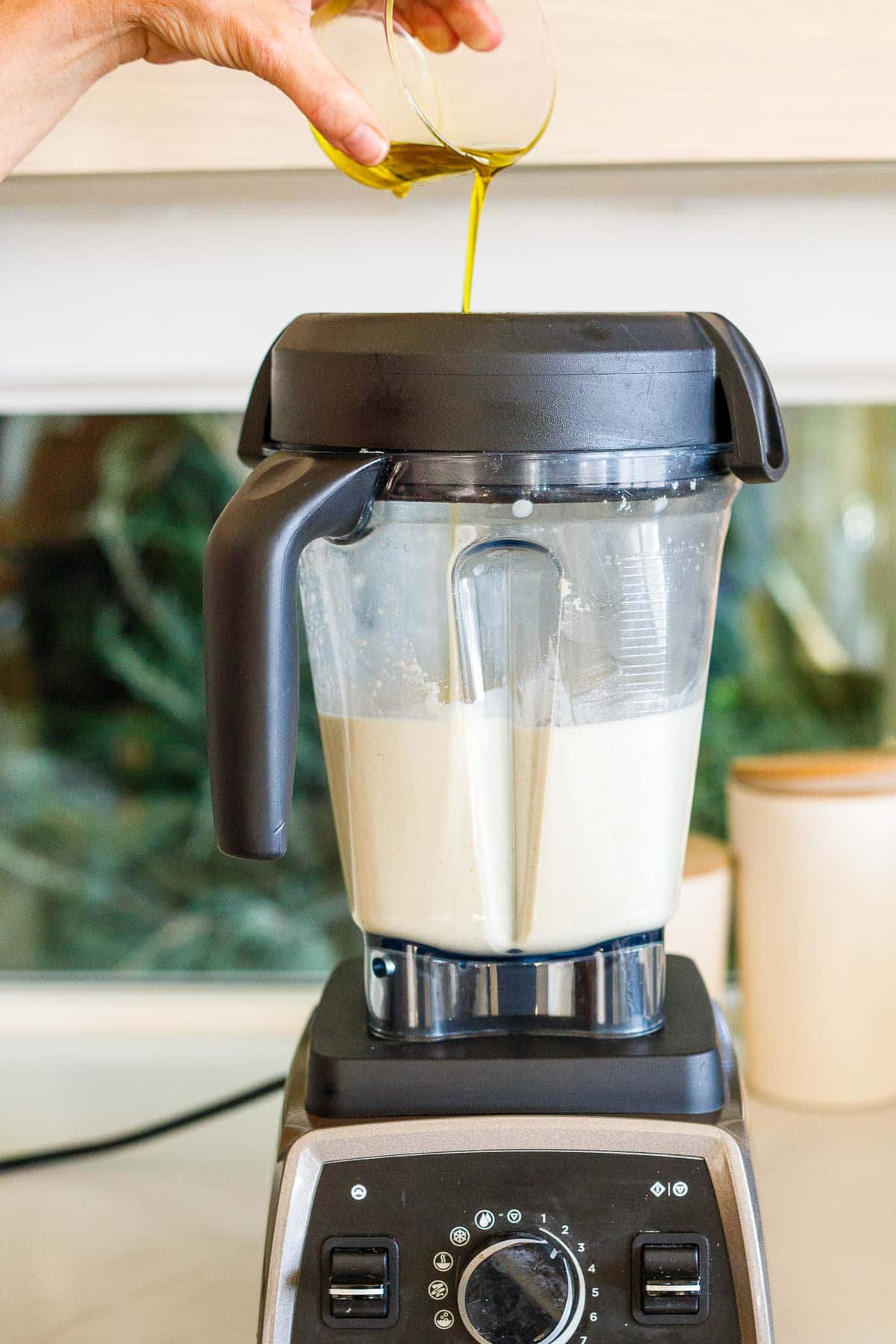 hand pouring olive oil into vitamix blender while making ajo blanco.