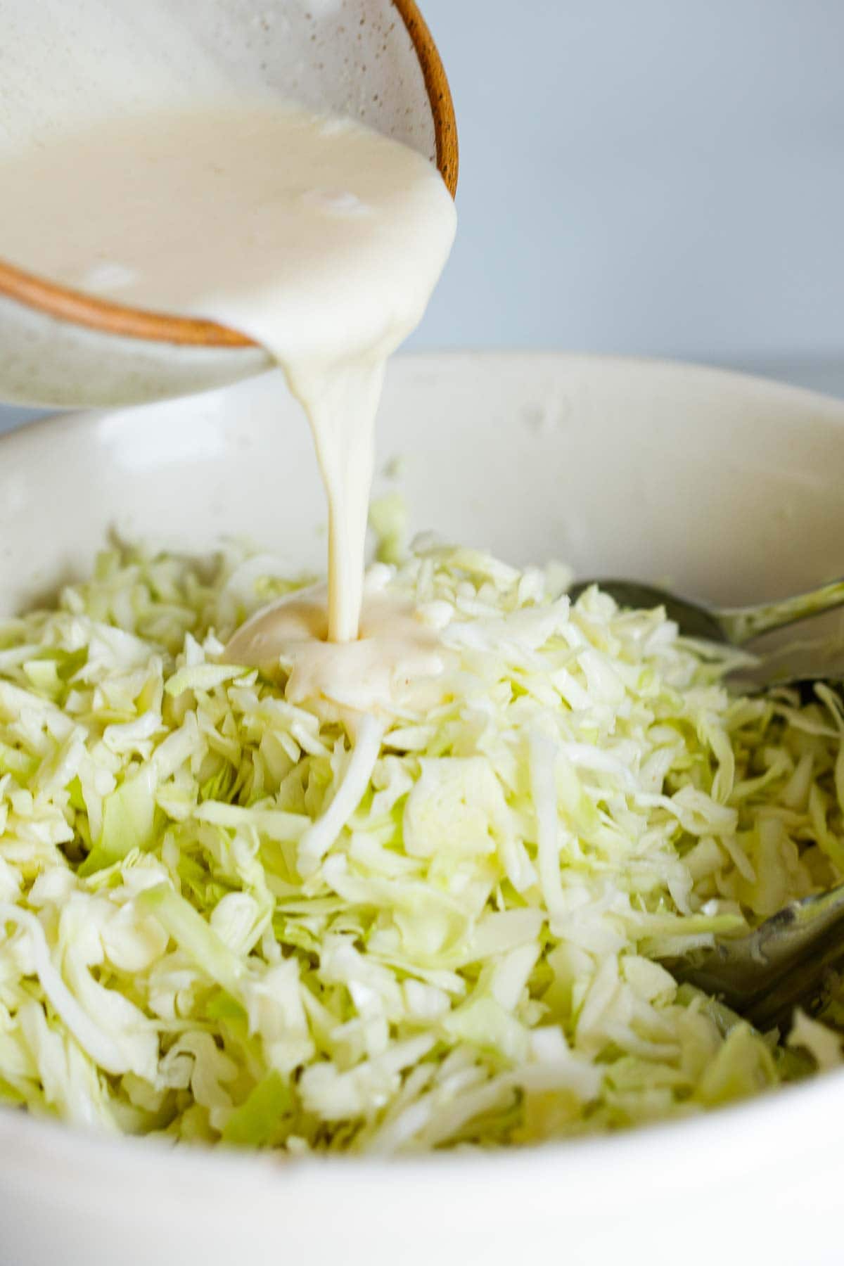 pouring creamy coleslaw dressing into large bowl of shredded green cabbage. 