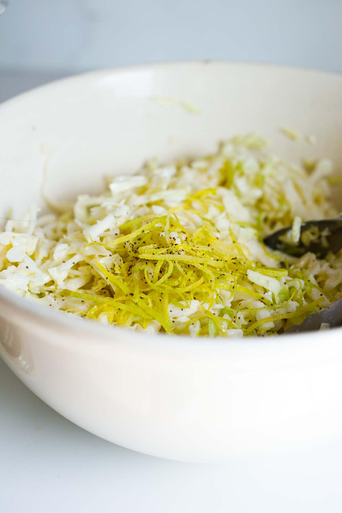 lemon zest and celery seeds on top of bowl of shredded green cabbage. 