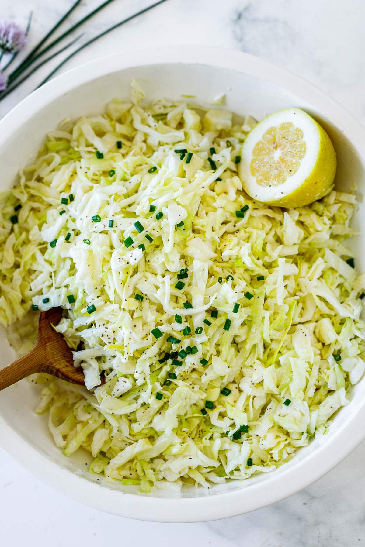 creamy coleslaw in a large bowl with wooden spoon and lemon halve. 